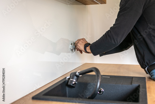 An electrician plugs in a socket built into the glass backsplash, building a new modern kitchen