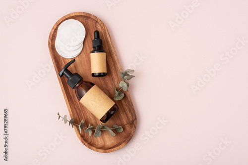 Brown glass cosmetic bottle and cotton pads on a wooden tray.