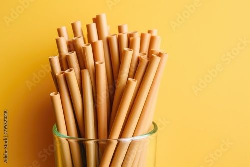 A collection of brown biodegradable pasta straws in a clear glass container on a yellow background. Brown Pasta Straws in Glass Container