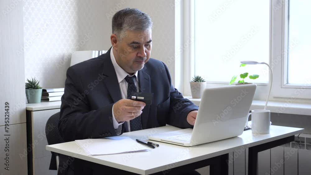 A businessman in a suit inputs bank card details on a computer. Suitable for online banking and internet shopping content. A businessman in a suit inputs bank card details on a computer. Suitable for online banking and internet shopping content.