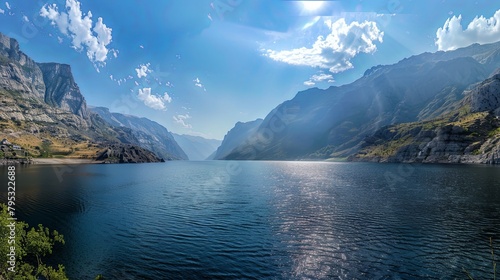 A panoramic vista of a wide and expansive lake nestled among towering mountains, with sunlight dappling the water's surface and creating a picturesque scene of natural beauty photo