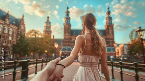 Romantic follow-me shot of woman leading partner's hand towards Amsterdam's historical center during sunset. 