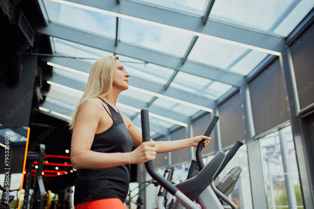 Side view photo of elderly woman exercising on training machine in modern health club for retirements. Woman staying healthy with exercise. Concept of sport, active seniors in modern lifestyle. Ad Side view photo of elderly woman exercising on training machine in modern health club for retirements. Woman staying healthy with exercise. Concept of sport, active seniors in modern lifestyle. Ad