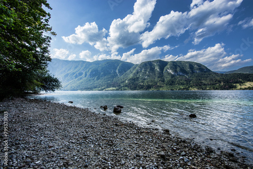 Ampia visuale panoramica della sponda nord del lago di Bohinj, in Slovenia e del suo bellissimo ambiente naturale circostante, sotto un cielo parzialmente nuvoloso, illuminato dal sole, in estate photo