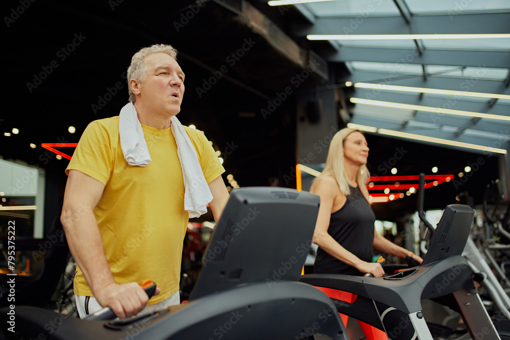 Senior fitness enthusiasts engaged in treadmill session at modern fitness center. Active older couple staying fit with gym workouts. Concept of sport, active seniors in modern life, healthy lifestyle.