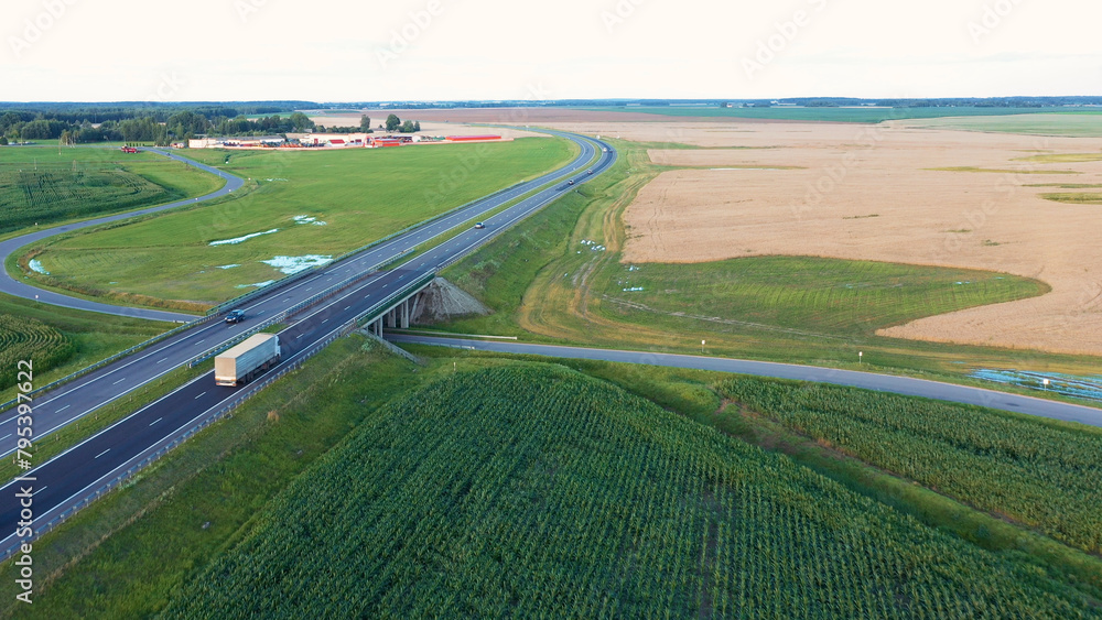 Long haul semi truck driving on intercity highway bridge in rural region. Agricultural grain corn grass wheat fields. Stage of delivery and logistics goods, aerial motion. Transportation and shipping