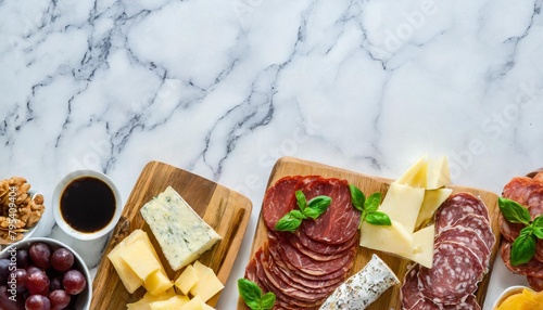 assortment of charcuterie cheeses meats and appetizers top view bottom border on a white marble background with copy space