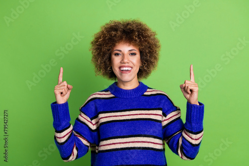 Portrait of cute girl with perming coiffure dressed knit pullover indicating at discount empty space isolated on green color background