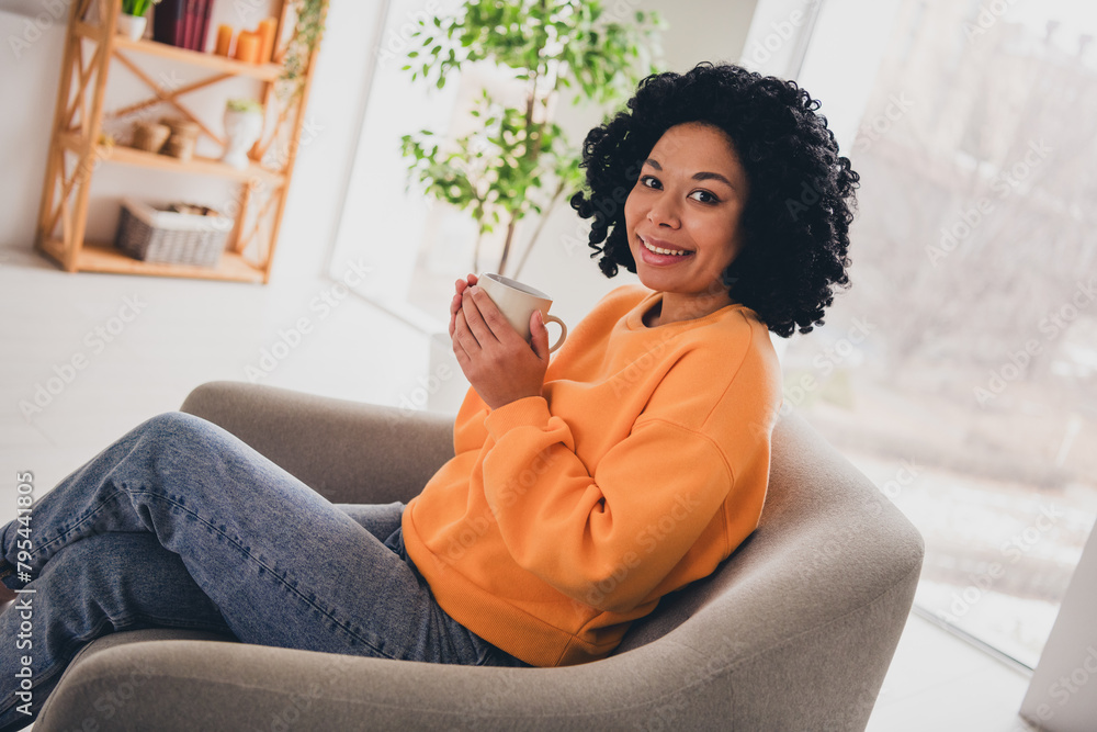 Photo portrait of lovely young lady sit armchair hold coffee dressed casual orange clothes cozy day light home interior living room - obrazy, fototapety, plakaty 