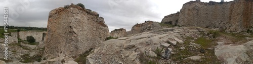 A stunning natural landscape with rock formation, lush greenery, and water, under cloudy skies.