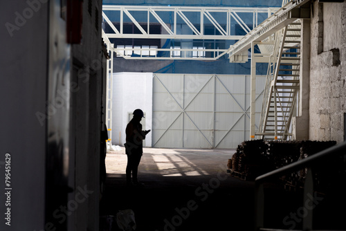 An expansive interior view of a large industrial warehouse with a silhouette of a person standing under the skylights, creating a dramatic and moody atmosphere