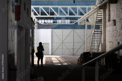 An expansive interior view of a large industrial warehouse with a silhouette of a person standing under the skylights, creating a dramatic and moody atmosphere