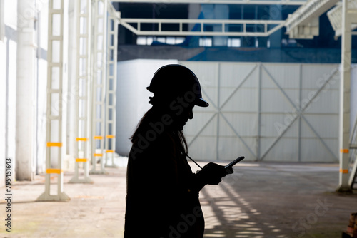A silhouetted figure stands in a spacious industrial interior, holding a tablet, with beams of light highlighting the surrounding structures
