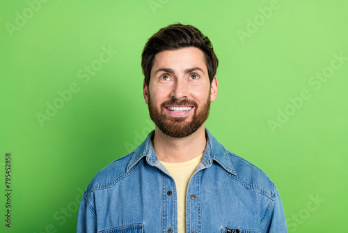 Photo of cheerful positive guy dressed jeans shirt smiling looking up empty space isolated green color background © deagreez