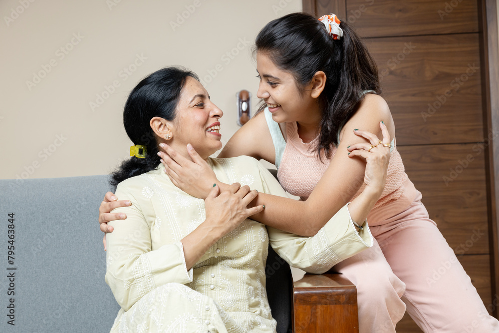 Indian Mother and Teen young daughter sitting on sofa at home looking towards the camera ,Happy Young teen hug Mother in living room having candid moments Indian Mother and Teen young daughter sitting on sofa at home looking towards the camera ,Happy Young teen hug Mother in living room having candid moments