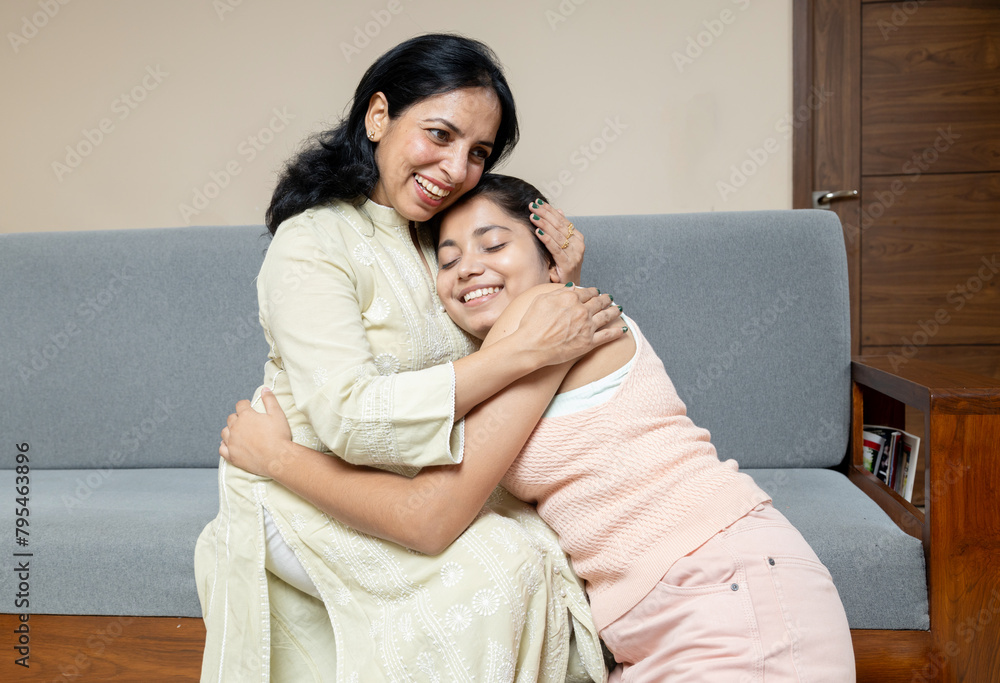 Mother hug Teenage daughter and Supporting her ,Indian Mother hug Teenage young girl sitting on sofa at living room,