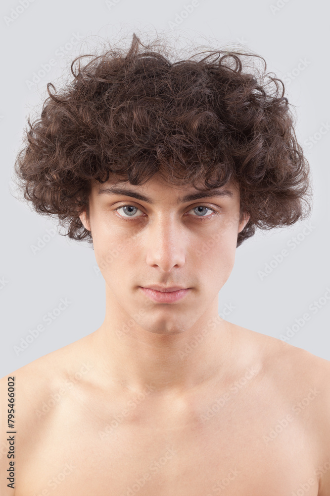 Smiling and handsome, a young man with curly hair, he looks into the camera with his blue eyes, a portrait of a guy with a bare chest isolated against a gray background Smiling and handsome, a young man with curly hair, he looks into the camera with his blue eyes, a portrait of a guy with a bare chest isolated against a gray background