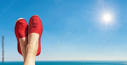 Damenbeine mit Roten Stoffschuhen vor blauem Himmel