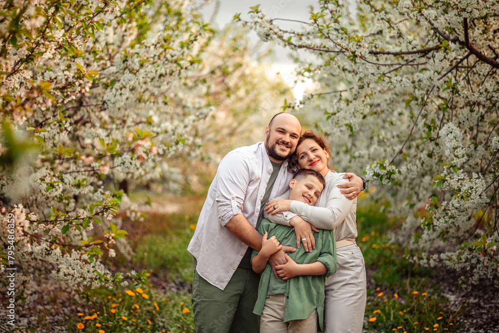 Happy family mom dad and teenager boy having fun on a spring walk in a blooming park Happy family mom dad and teenager boy having fun on a spring walk in a blooming park