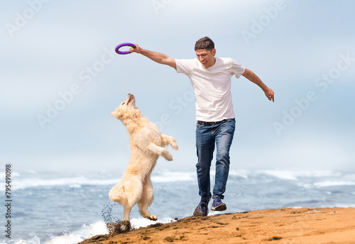 A happy owner and his golden retriever play on the sandy beach on a sunny summer day. Life with a dog concept. Summer with dog