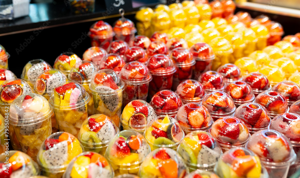 Fruit Salad arranged in plastic cups on a market. Cut and ready fruit ready to sell in market. Convenience, healthy lifestyle. Strawberries, kiwi, melon, pineapple, figs, dragon in a plastic glass.