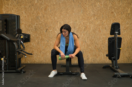 Young, beautiful, brunette woman with yellow top, black leggings and towel around her neck, tired and exhausted after exercise, sitting on a bench in the gym. Fitness concept, gymnastics, bodybuilding photo