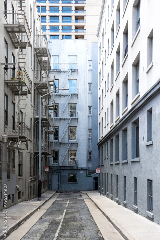 Backyard in downtown San Francisco (USA). Facades, balconies, windows, floor and walls of city houses in shades of grey, white and pale blue. Dead end small road with vanishing point perspective.