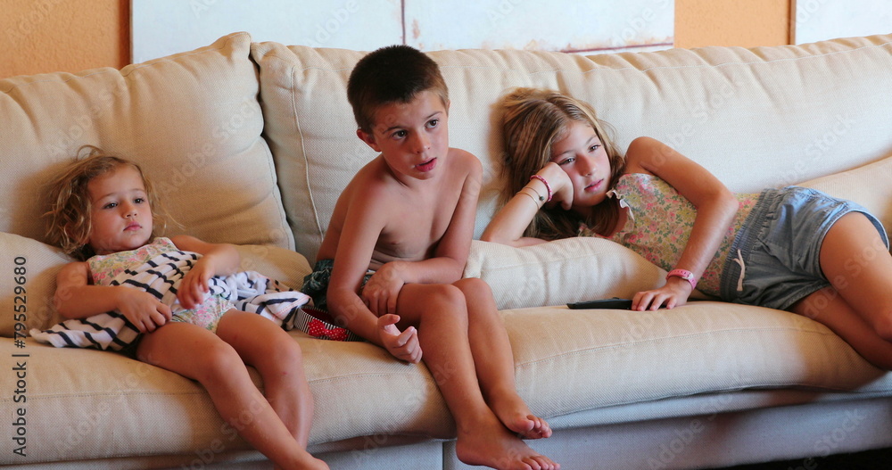 Obraz premium Children seated at sofa watching movie screen at home