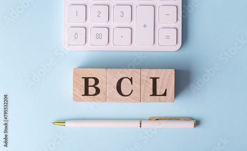 BCL word on wooden block with pen and calculator on blue background photo