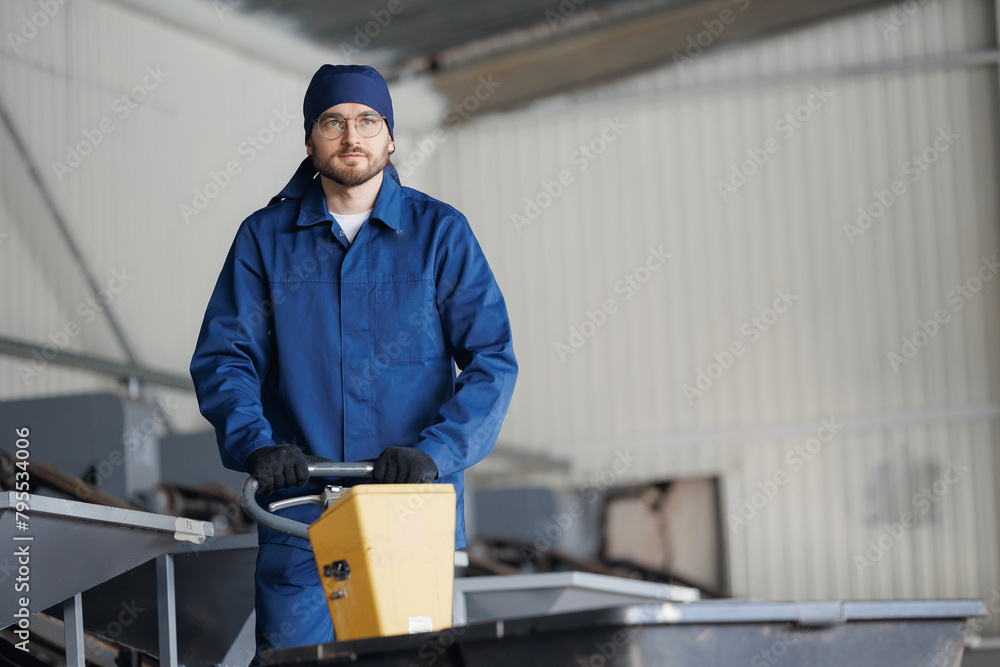 Young man worker with blue uniform with trolley for transporting cedar nuts. Concept modern food industry, factory production line Young man worker with blue uniform with trolley for transporting cedar nuts. Concept modern food industry, factory production line