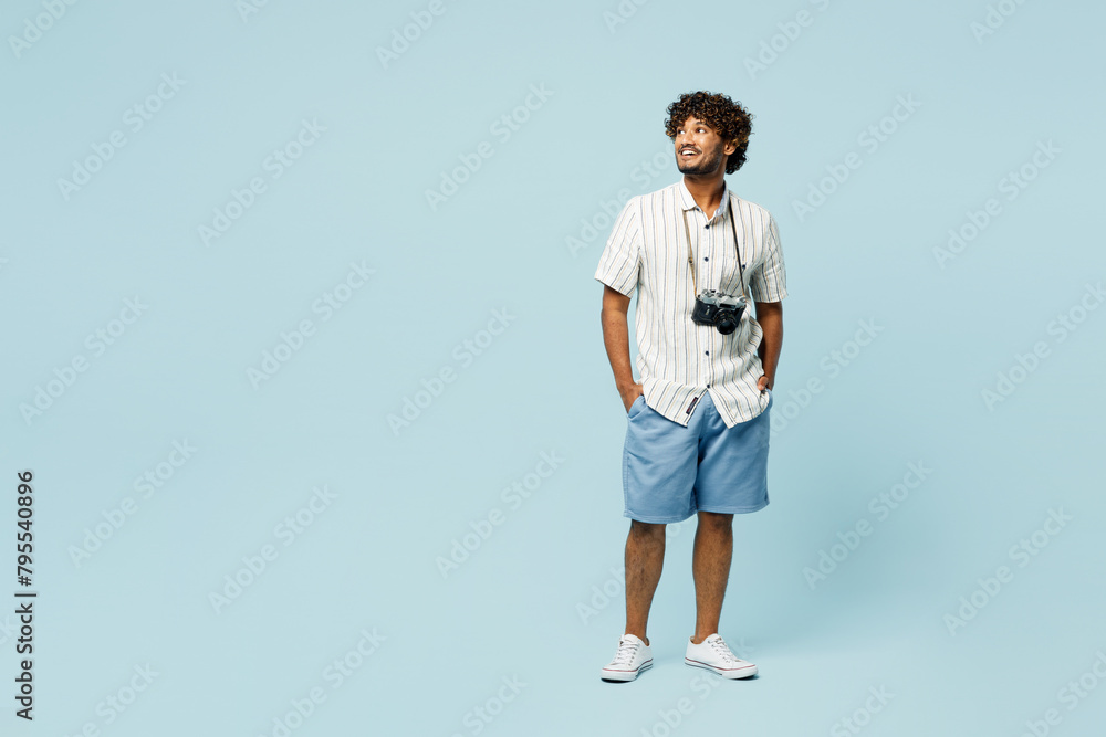 Full body traveler Indian man wears white casual clothes look aside on area isolated on plain blue background. Tourist travel abroad in free spare time rest getaway. Air flight trip journey concept. Full body traveler Indian man wears white casual clothes look aside on area isolated on plain blue background. Tourist travel abroad in free spare time rest getaway. Air flight trip journey concept.