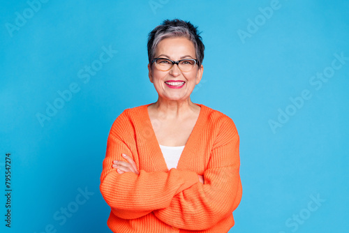 Photo of aged lady toothy smile crossed arms wear orange cardigan isolated on blue color background