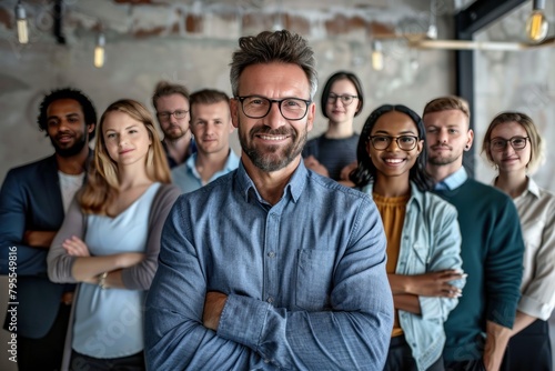 A group of people are smiling and posing for a photo. The man in the center is wearing glasses and has a big smile on his face. The group is diverse, with people of different ages and races photo