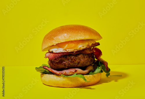 Hamburger with bacon and egg in a brioche bun on a yellow background. © Mark