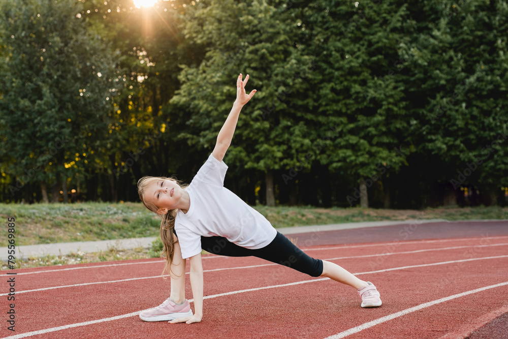 Tween girl stretching while jogging on a running track. Sport, healthy lifestyle, physical education.