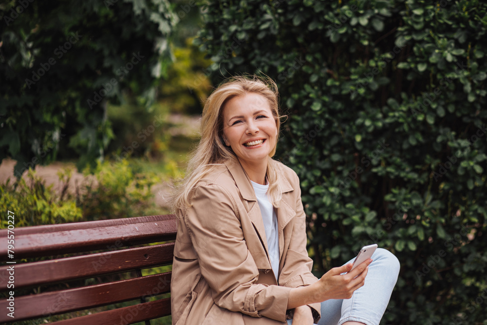 Closeup portrait of a smiling happy young woman with smartphone against the greenery of a city park Closeup portrait of a smiling happy young woman with smartphone against the greenery of a city park