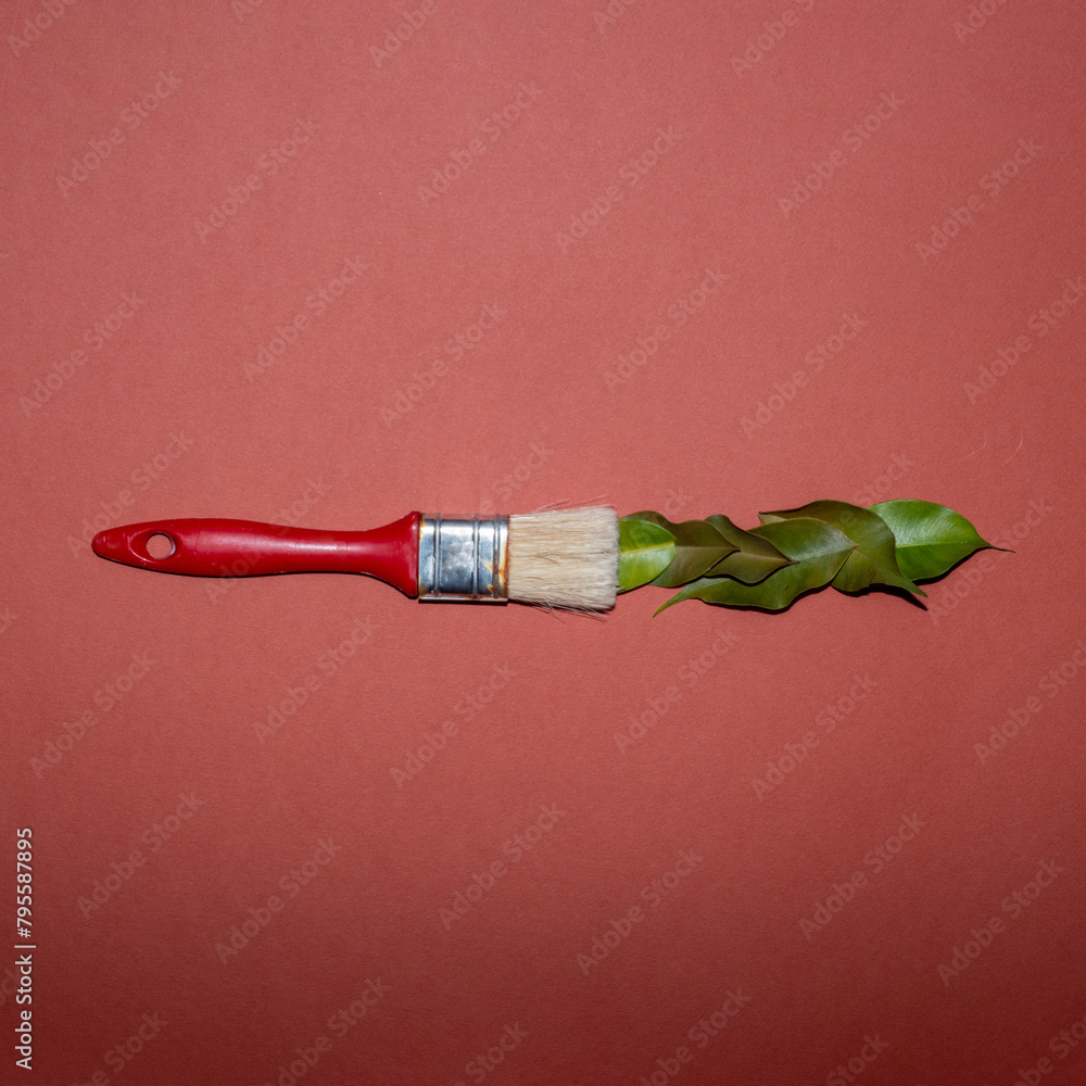 Fototapeta premium Red paintbrush and green leaves creative flat lay concept on an orange background.