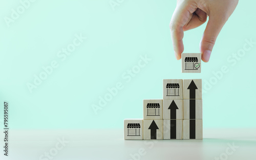 Business growth and franchise expansion concept. Hand stacking wooden blocks with store icons, depicting strategy of business growth and franchise expansion. increasing store on digital upward trend