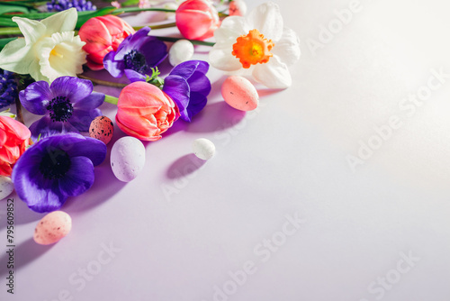 Happy Easter mockup. Easter eggs with spring pink purple flowers flat lay on purple background. Greeting card or banner.