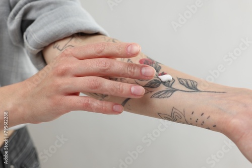 Tattooed woman applying cream onto her hand on light background, closeup