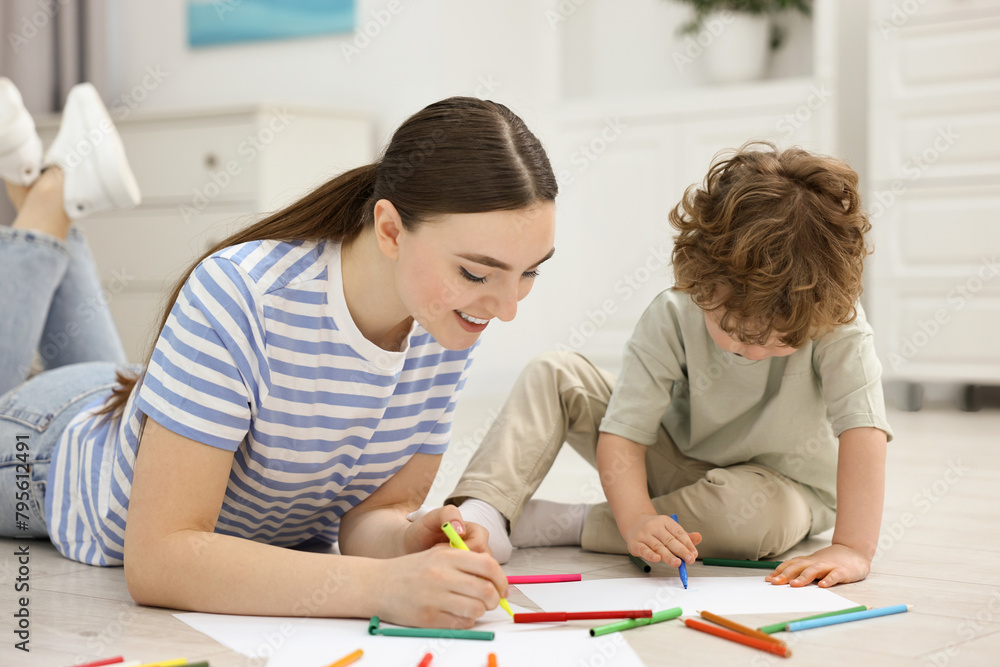Mother and her little son drawing with colorful markers on floor at home Mother and her little son drawing with colorful markers on floor at home