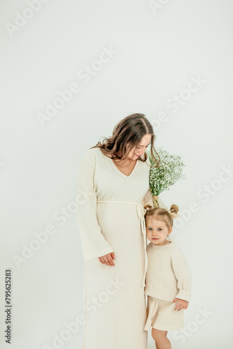 Beautiful young pregnant woman with her little 3 yearold daughter on white background. Stylish pregnant woman in beige dress. Motherhood. Mother's Day. photo