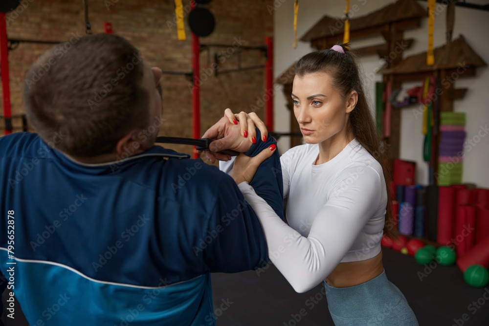 Obraz premium Young athletic woman performing self-defense move during training sparring