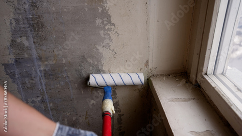 A man builder priming a wall before doing further work with a construction roller. Priming the wall with a roller, apartment renovation concept. A man paints a wall with a roller.