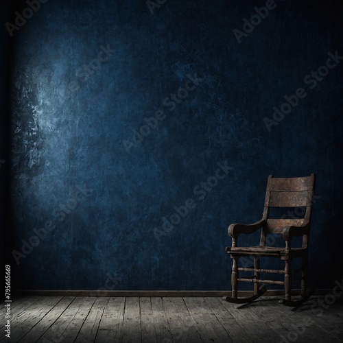 Single wooden rocking chair sits in middle of dark room with blue walls, wood floor. Beam of light shines down from left side of image, illuminating chair, small portion of wall, floor.