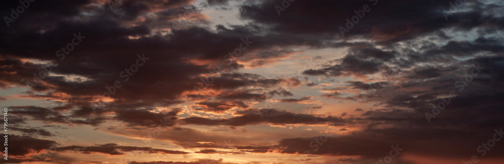 Sunset in the summer field. The clouds in the sky are lit by the setting sun on the horizon. The blue sky changes color in the rays of the sun at sunset. Clouds in the sky above the horizon.