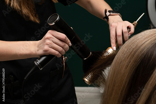 Beauty sphere. The master hairdresser does styling and combing the hair. Combs a client's long hair with a round brush and blow-dries it in a beauty salon. Close-up. Business concept.
