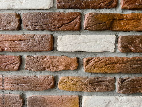 Brick wall with brown, white bricks close-up. The texture of the bricks is rough and uneven, with visible cracks and chips and cement between the bricks