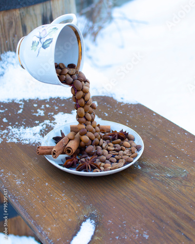 Winter decor and coffee grains on a on a dark, snowy table. The grains fall from the cup. Spiced coffee. Winter hot drink.