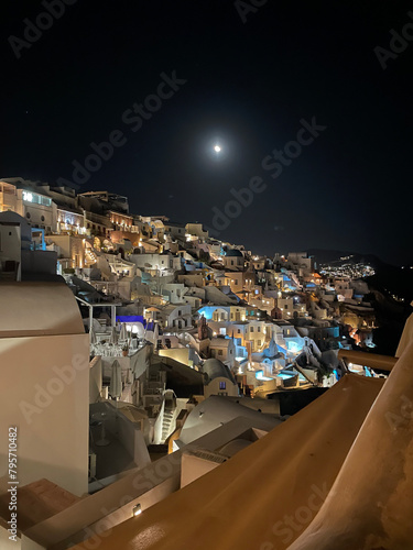 Oia village in Santorini, Greece at nighttime with moon and lights from hotels and restaurants